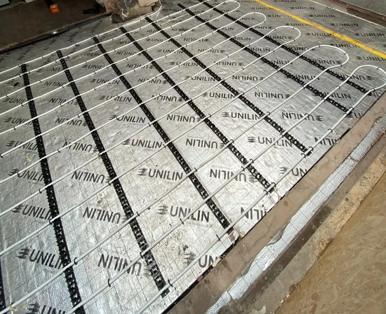 Underfloor heating pipe loops secured across insulated flooring by DPB